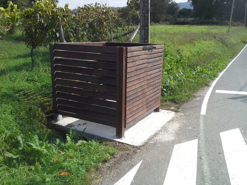 Cubrecontenedor de lamas de madera junto a una carretera