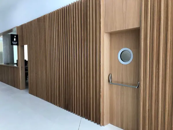 Wooden fire door with a porthole window and panic bar, set into a slatted wall lining at the Pontevedra courts