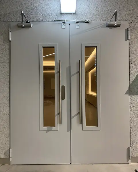 Grey double metal door with vertical glazing, pull handles and overhead door closers